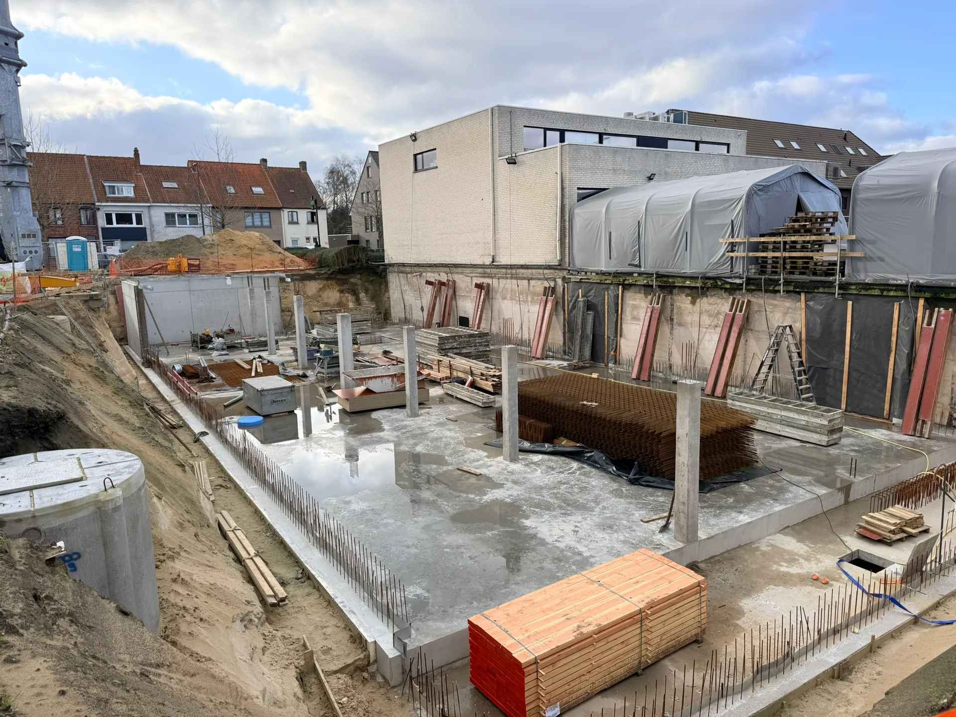 Keldervloer met betonkolommen, wachtwapening, een stapel wapeningsnetten en bekistingsbalken in een bouwput