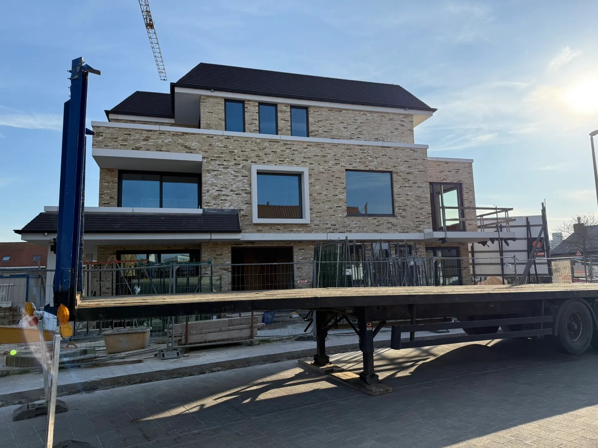 Wind- en waterdicht woongebouw met genuanceerde gevelsteen, donker pannendak en geplaatste ramen, met torenkraan erachter