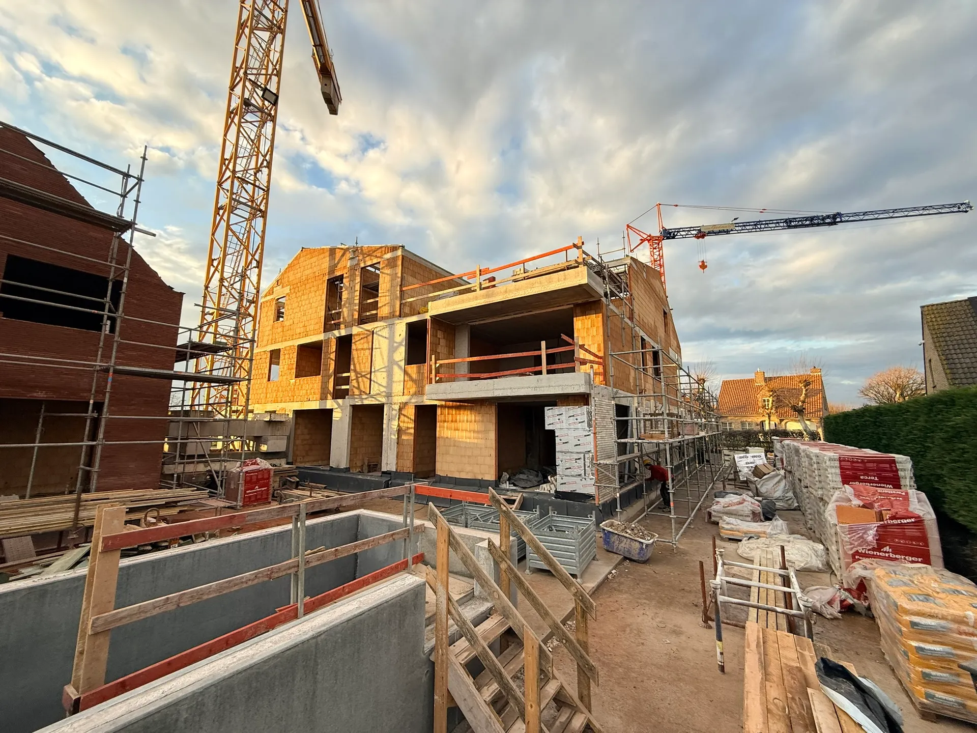 Achterzijde van een appartementsgebouw in snelbouwsteen met steiger, twee kranen en op de voorgrond betonwanden met een houten werftrap