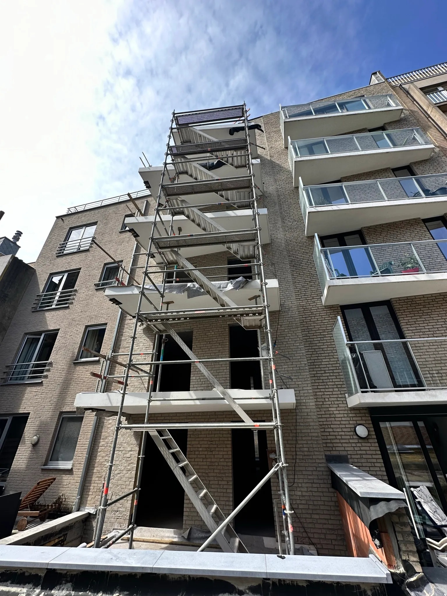 Steigertoren met trappen tegen de bakstenen achtergevel van een appartementsgebouw met betonnen balkons en glazen borstweringen