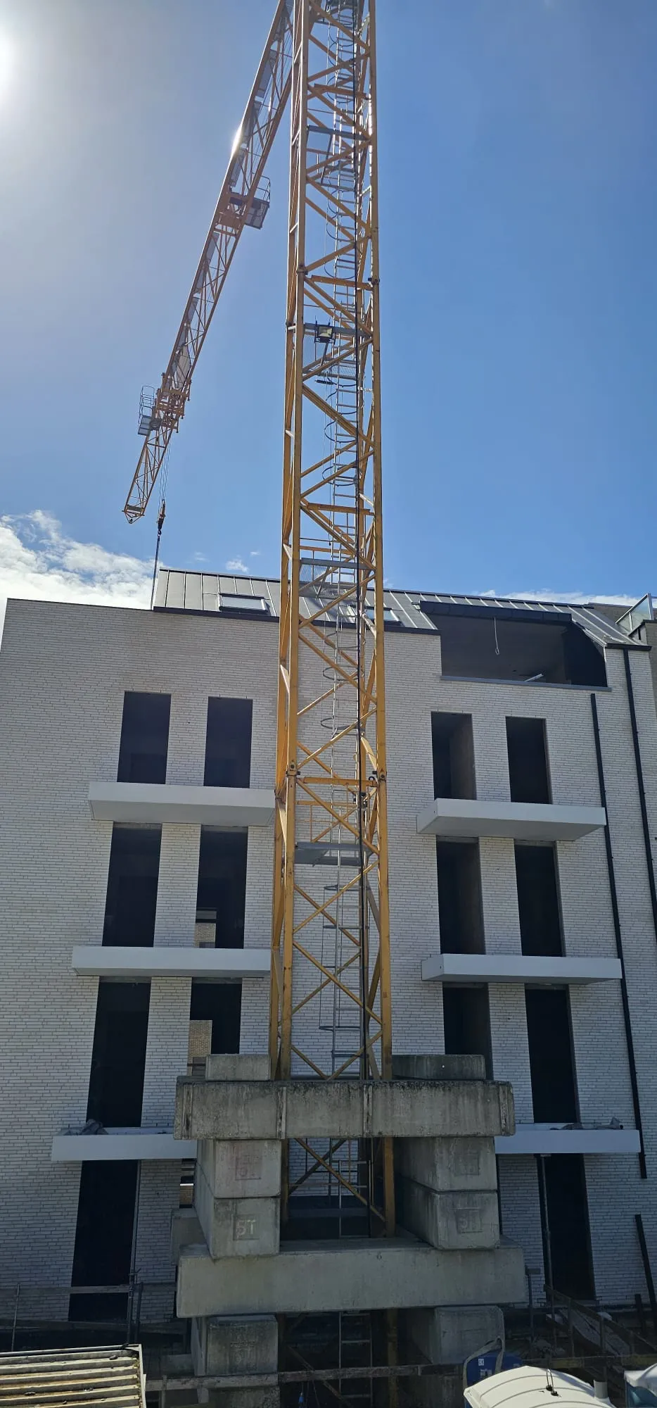 Gele torenkraan met betonnen ballastblokken voor de witte bakstenen gevel van een appartementsgebouw met betonnen balkons