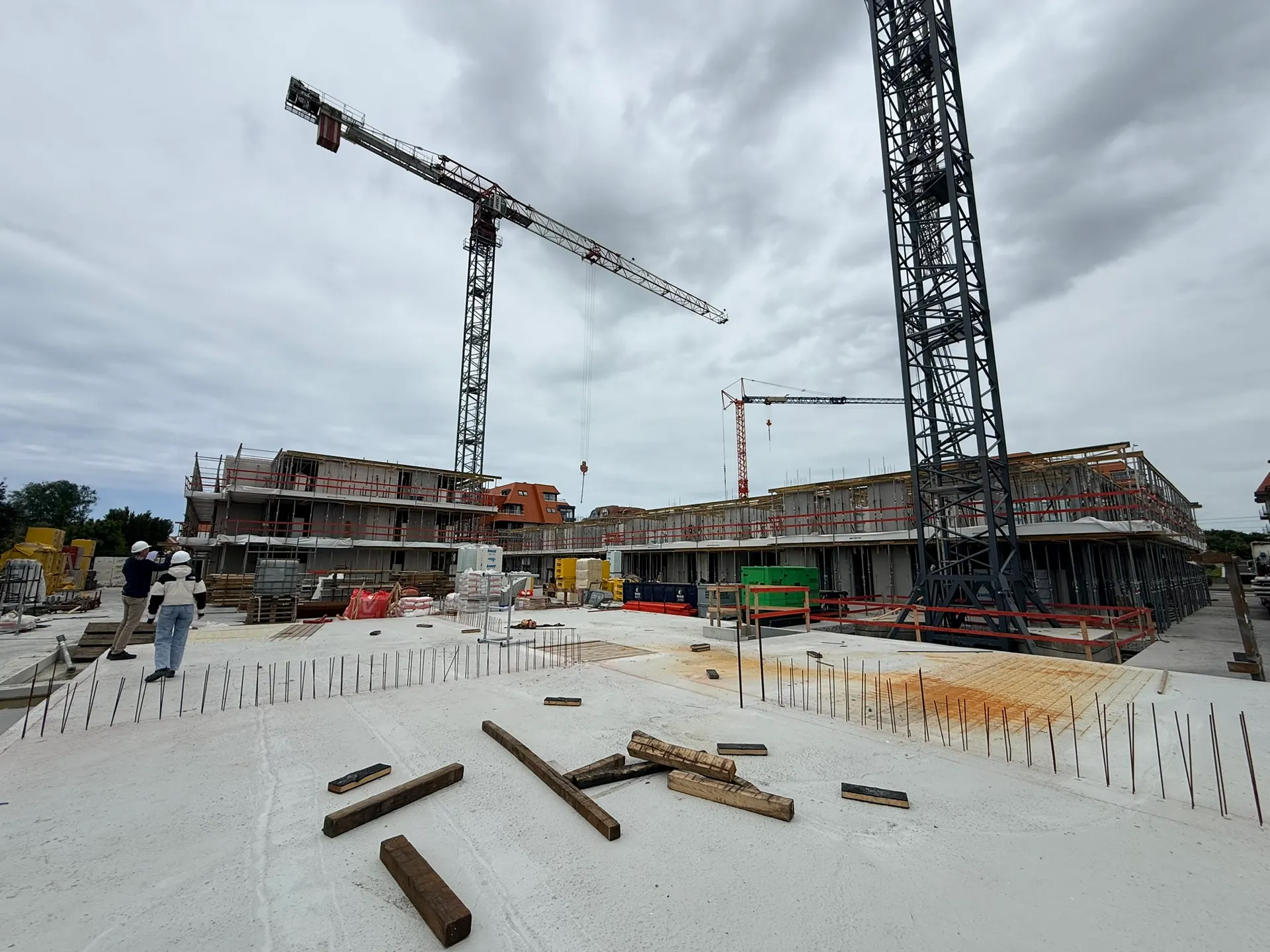 Betonnen vloerplaat met wachtwapening en drie torenkranen, terwijl twee personen met witte helm de werf overschouwen