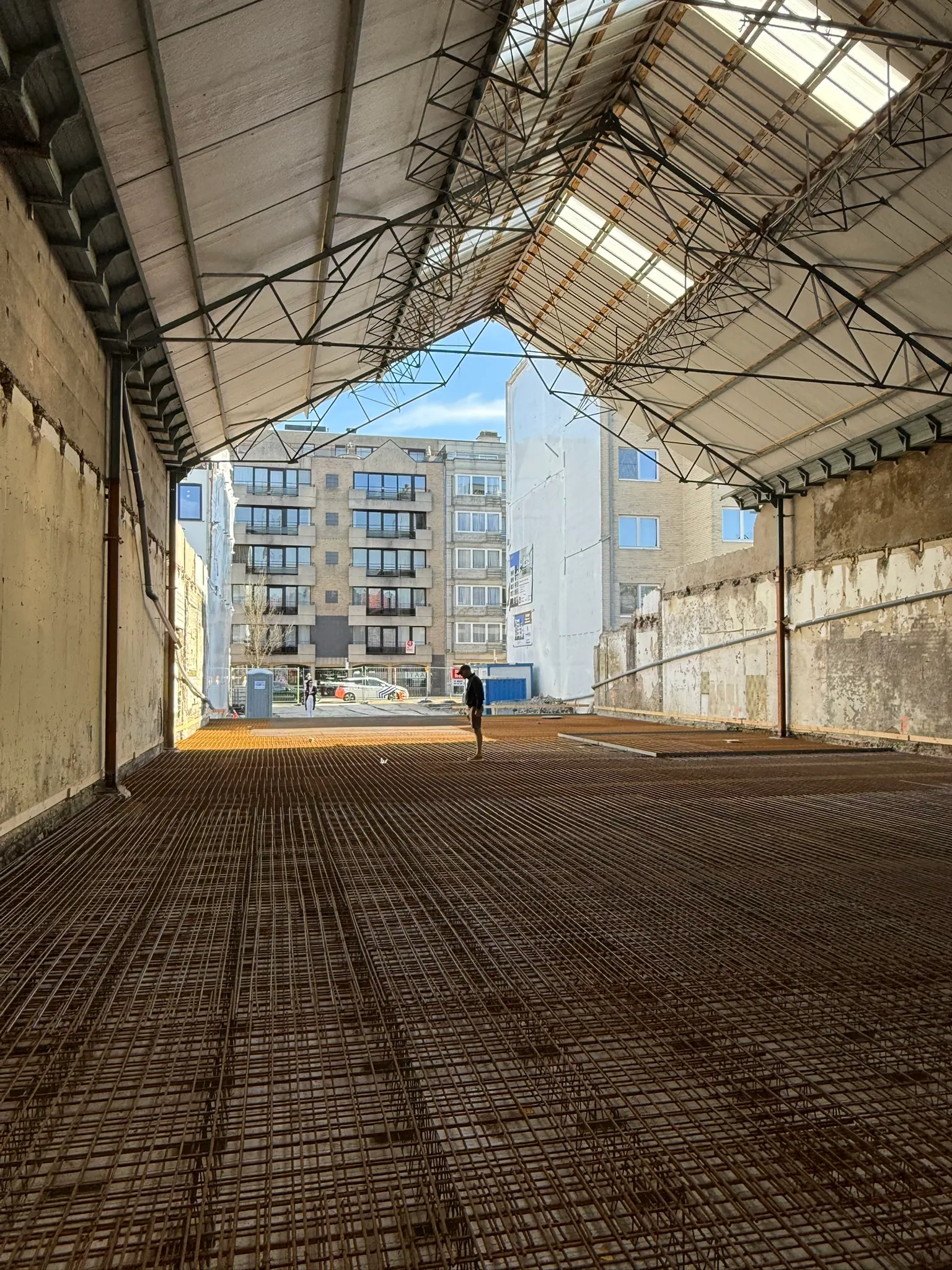 Grote vloer vol wapeningsnetten onder de stalen dakspanten van een bestaande loods, klaar voor de betonstort