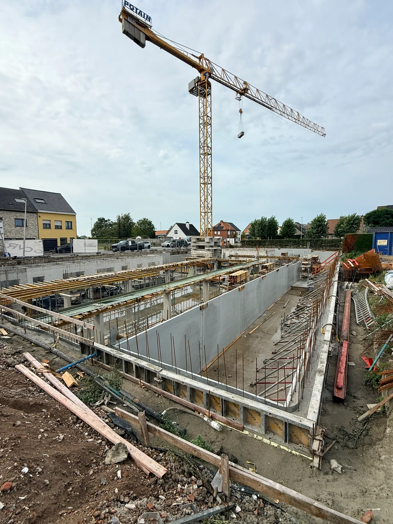 Geschoorde prefab betonwanden in een kelder, met houten onderslagbalken voor de vloerplaat en een torenkraan erboven