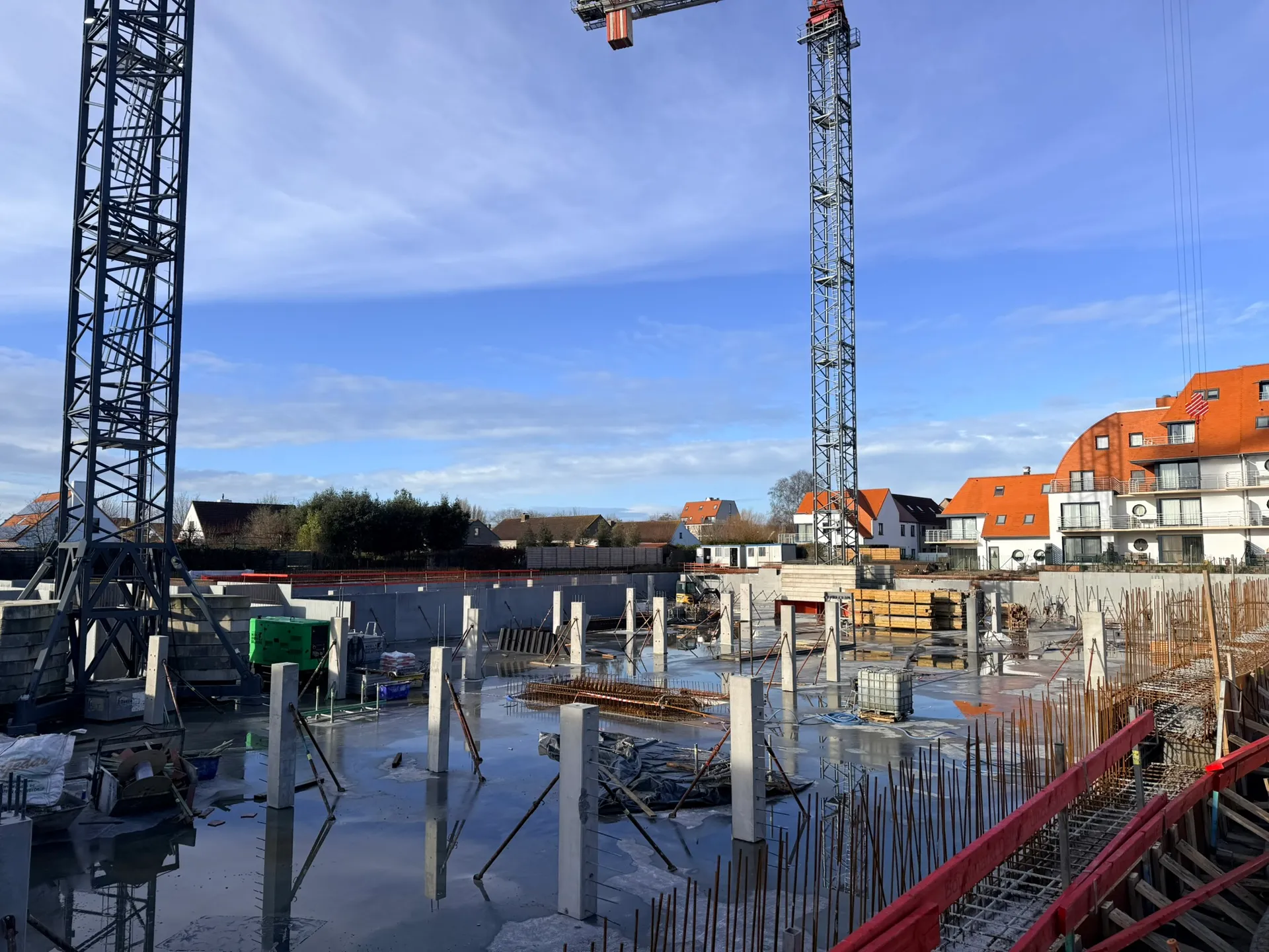 Rij geschoorde betonkolommen op een natte vloerplaat, met wachtwapening, rode randbekisting en twee torenkranen