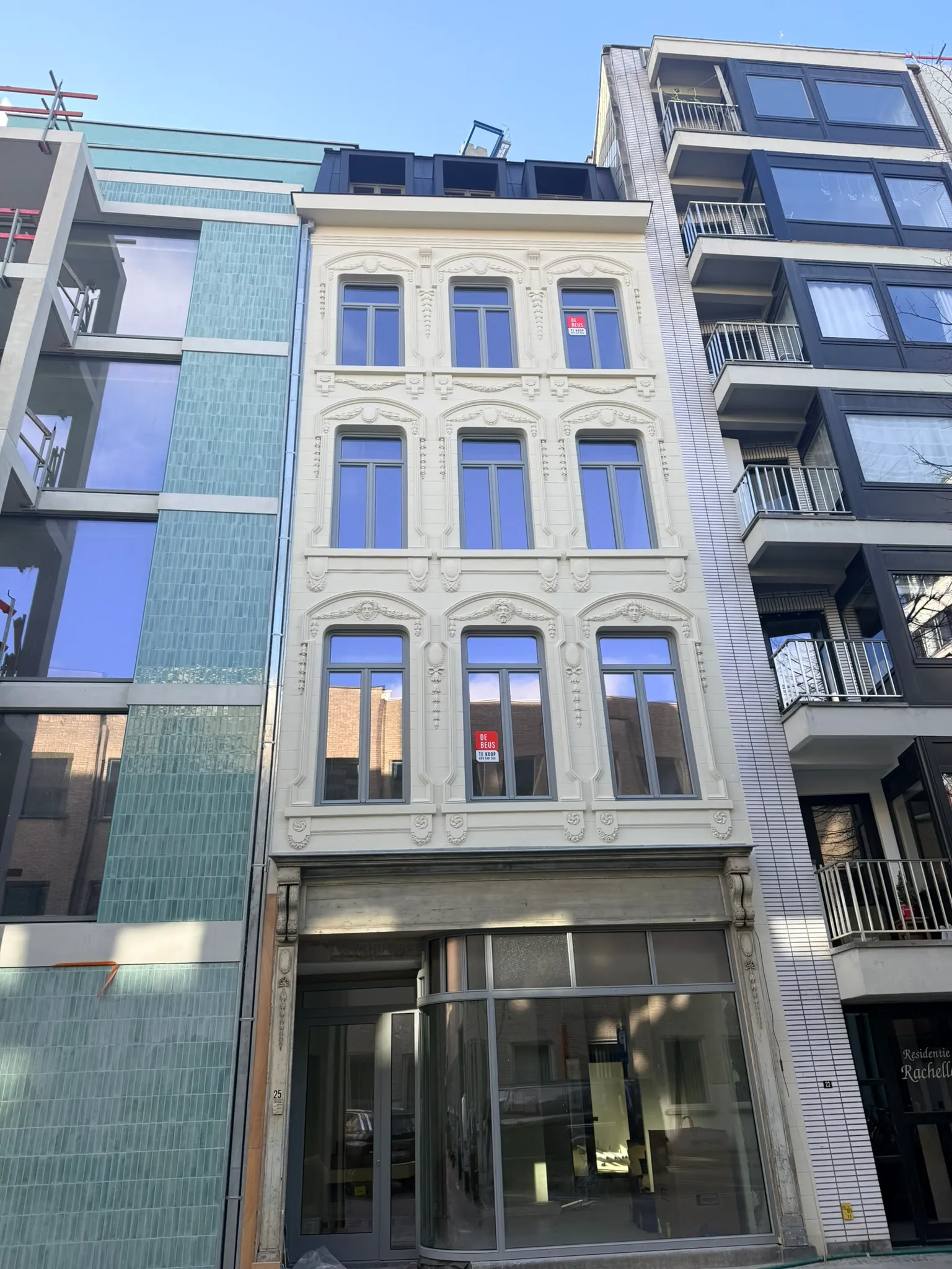 Gerestaureerde witte historische gevel met ornamenten en nieuwe ramen, naast een nieuwbouwgevel in groene geglazuurde steen